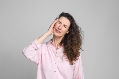 Mature woman suffering from headache on light grey background