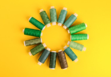 Different shades of green sewing threads on yellow background, flat lay. Space for text