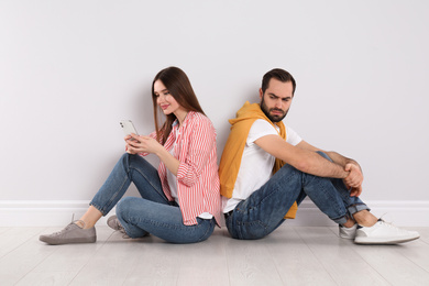 Distrustful young man peering into girlfriend's smartphone indoors. Relationship problems