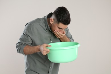 Man with basin suffering from nausea on beige background. Food poisoning