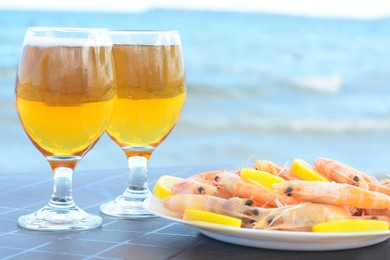 Photo of Cold beer in glasses and shrimps served with lemon on beach, closeup