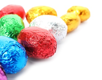 Many chocolate eggs wrapped in bright foil on white background, closeup