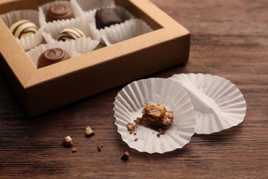Photo of Candy paper cups near partially empty box of chocolate sweets on wooden table, closeup