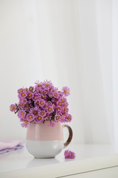 Cup with beautiful flowers on white table in light room
