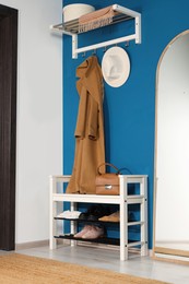 Photo of Stylish hallway with shoe storage bench and mirror near blue wall. Interior design