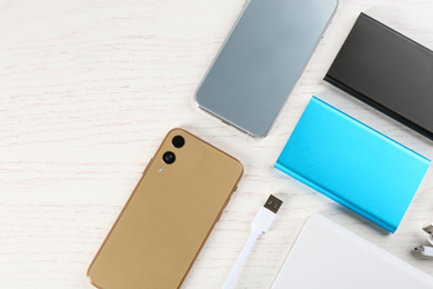 Flat lay composition with mobile phones and portable chargers on white wooden background