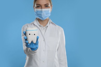 Dental assistant holding toy tooth with funny face against light blue background, focus on hand. Space for text