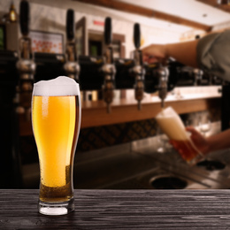 Fresh cold beer on wooden table and bartender in pub, space for text