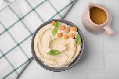 Delicious hummus with chickpeas served on white tiled table, flat lay