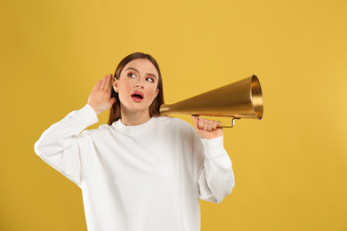 Emotional young woman with vintage megaphone on yellow background