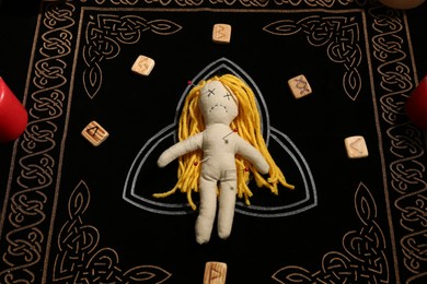 Voodoo doll pierced with pins and runes on black mat, above view. Curse ceremony