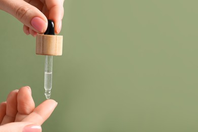 Woman dripping serum from pipette on her hand against olive background, closeup. Space for text