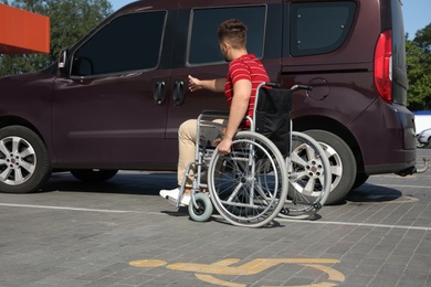 Young man in wheelchair opening door of van on car parking