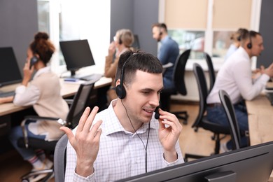 Photo of Call center operators working in modern office, focus on young man with headset
