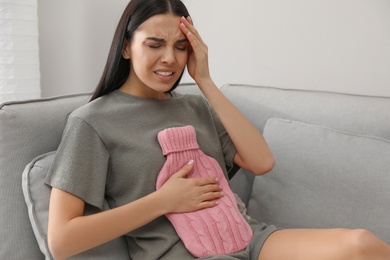 Woman using hot water bottle to relieve abdominal pain at home