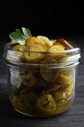 Photo of Glass jar with slices of pickled green jalapeno peppers on black wooden table