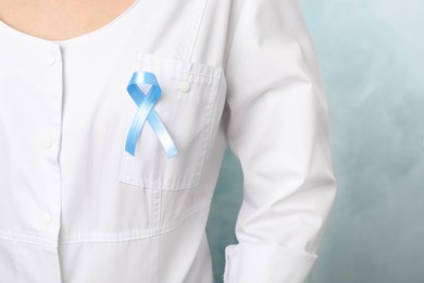 Photo of Doctor with light blue awareness ribbon on color background, closeup