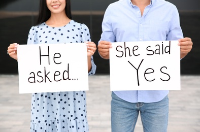 Lovely couple holding posters with text HE ASKED... SHE SAID YES after engagement outdoors, closeup