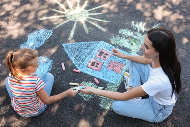 Cute little child and her mother drawing with colorful chalks on asphalt, above view