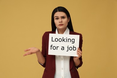 Photo of Unemployment problem. Unhappy woman holding sign with phrase Looking For A Job on pale orange background