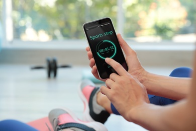 Young woman using fitness app on smartphone indoors, closeup
