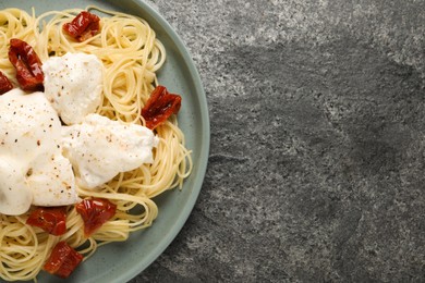 Delicious spaghetti with burrata cheese and sun dried tomatoes on grey table, top view. Space for text