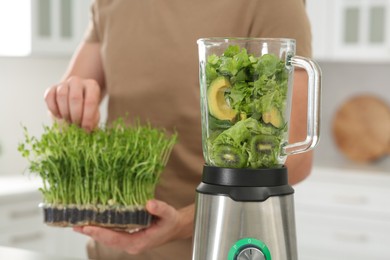 Photo of Man holding microgreen peas for delicious smoothie and blender with ingredients in kitchen, closeup