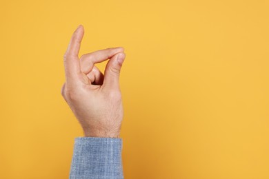Man snapping fingers on yellow background, closeup of hand. Space for text
