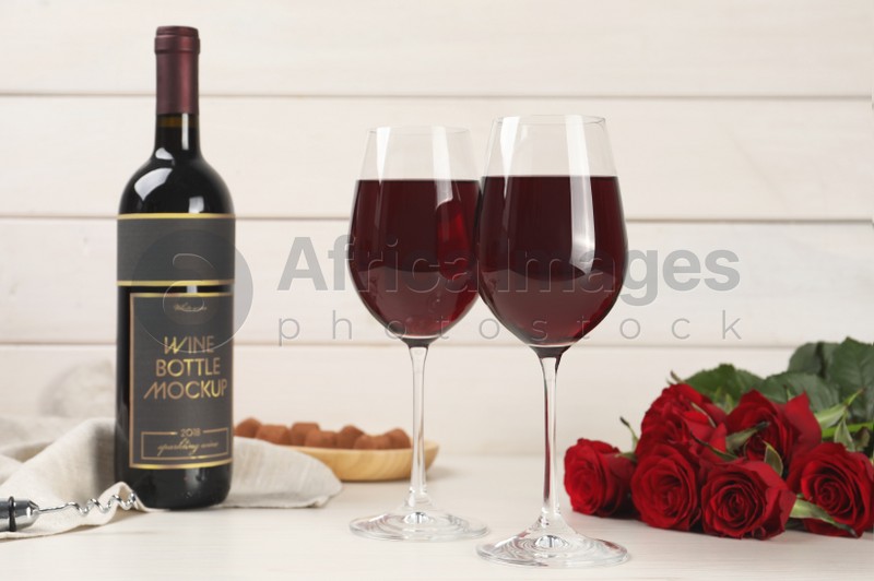 Photo of Bottle with glasses of red wine and beautiful roses on white wooden table