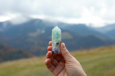 Woman holding beautiful crystal in mountains, closeup