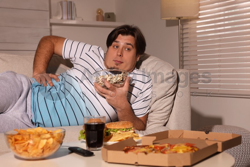 Overweight man with bowl of popcorn on sofa at home