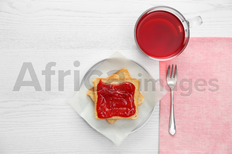 Tasty toast with jam and raspberry tea on white wooden table, flat lay. Delicious morning meal