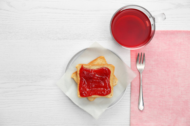 Tasty toast with jam and raspberry tea on white wooden table, flat lay. Delicious morning meal
