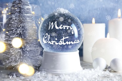 Image of Beautiful snow globe with phrase Merry Christmas and candles on table