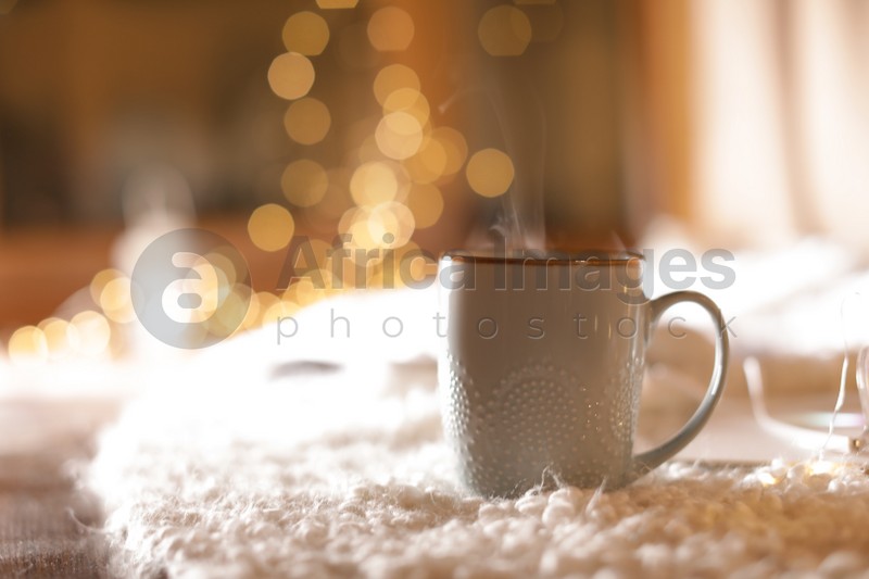 Cup of hot beverage on fuzzy rug against blurred background, space for text. Winter evening