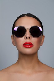 Attractive woman in fashionable sunglasses against grey background