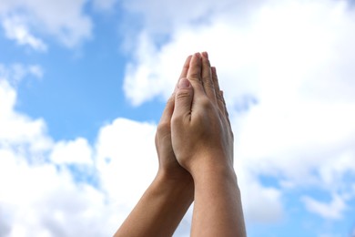 Woman with clasped hands praying against blue sky, closeup