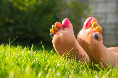Photo of Teenage girl with painted toes on green grass outdoors, closeup. Space for text