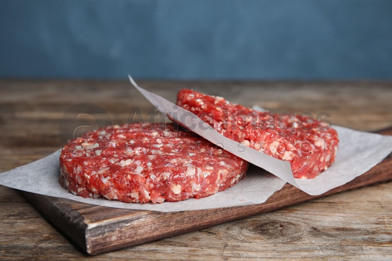 Raw meat cutlets for burger on wooden table against blue background