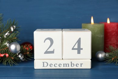 December 24 - Christmas Eve. Wooden block calendar and festive decor on blue table