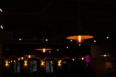 Lamps with glowing light bulbs in dark restaurant. Space for text