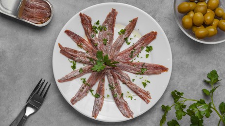 Photo of Delicious anchovy fillets, served with olives and parsley on grey table, flat lay