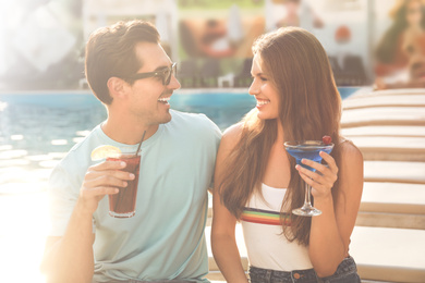 Image of Happy young couple with fresh summer cocktails relaxing near swimming pool
