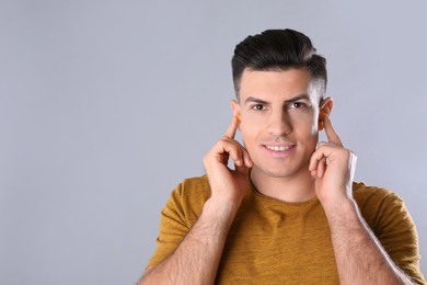 Man inserting foam ear plugs on grey background. Space for text