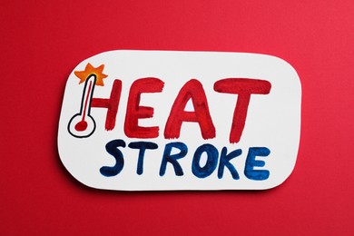 Card with words Heat Stroke and thermometer on red background, top view