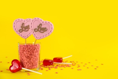 Heart shaped lollipops made of chocolate and sugar syrup with sprinkles on yellow background. Space for text