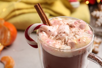 Photo of Delicious marshmallow drink with cinnamon and candy cane in cup on blurred background, closeup