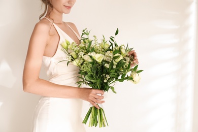 Young bride wearing wedding dress with beautiful bouquet on light background, closeup