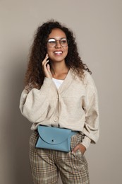Beautiful African American woman with stylish waist bag on beige background