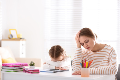 Upset mother and daughter doing homework together at table indoors